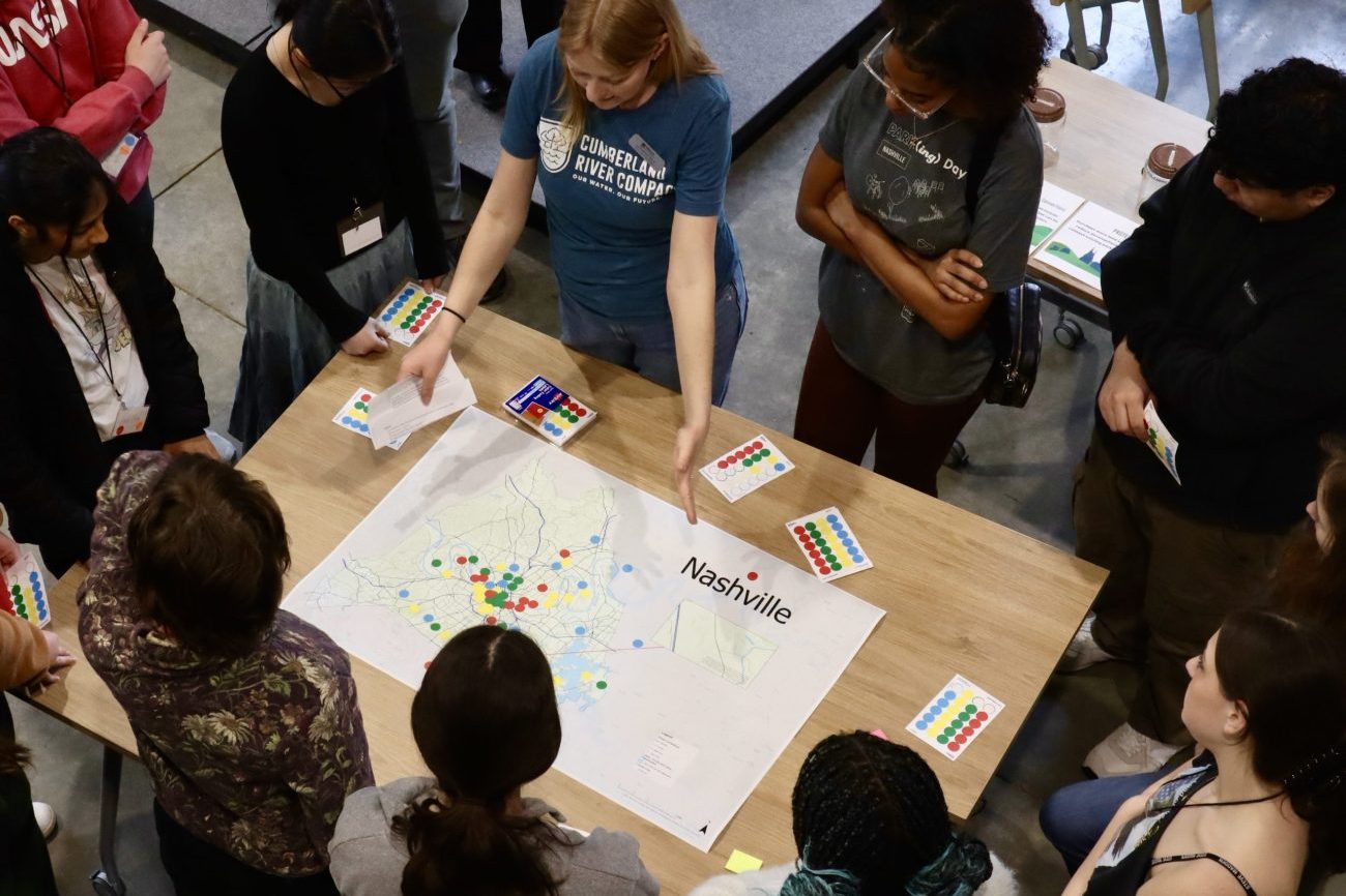 Compact staff standing with a group of students around a table with a map of Nashville.