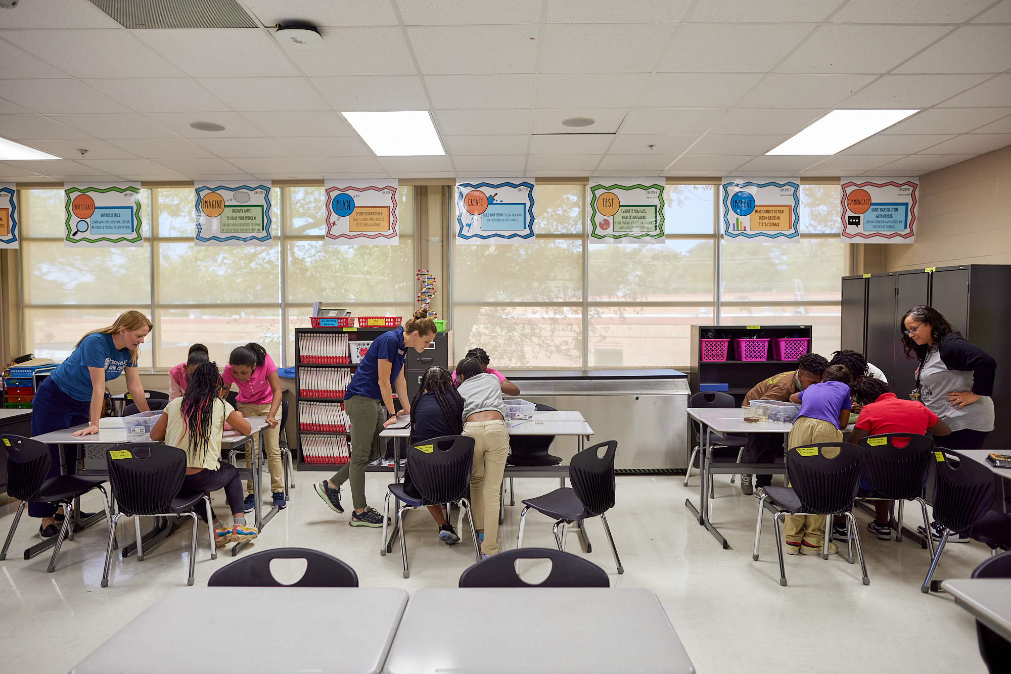 A classroom, with teachers and students leaning over different tables.